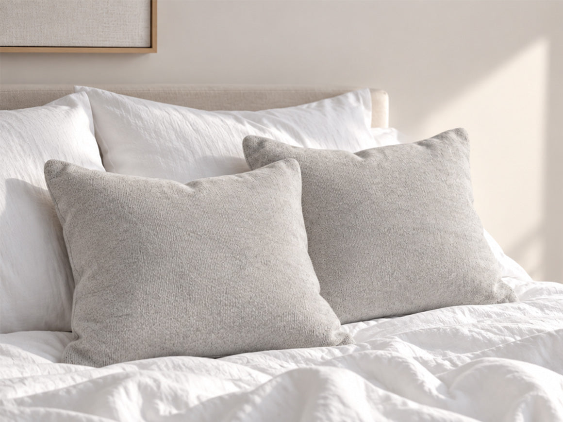 Coussin et couvre-lit en cachemire gris mis en scène avec une parure de lit claire dans une chambre contemporaine